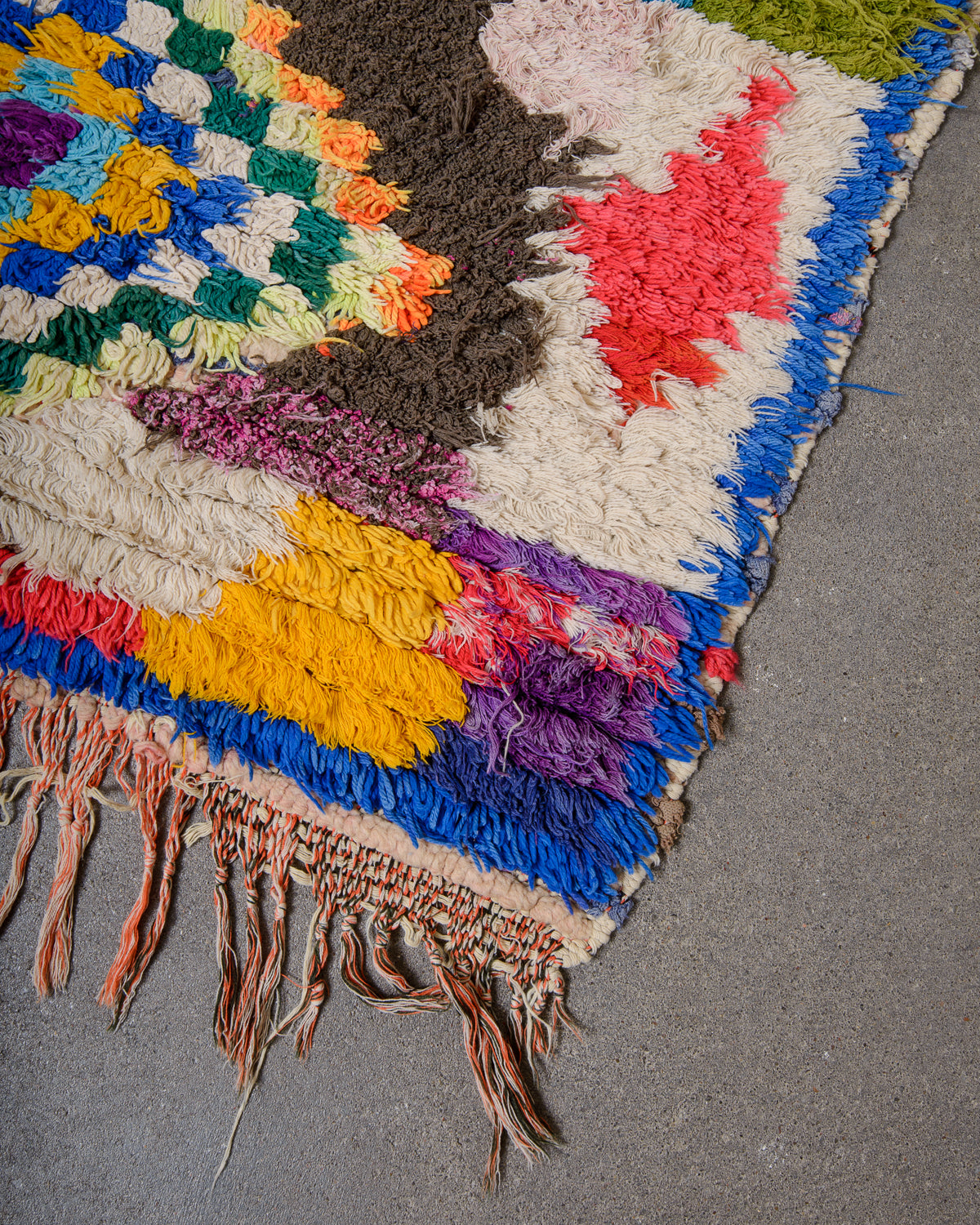 Corner of Berberlin vintage Boucherouite runner rug made of colourful cotton, wool and cloth, laying on concrete floor.